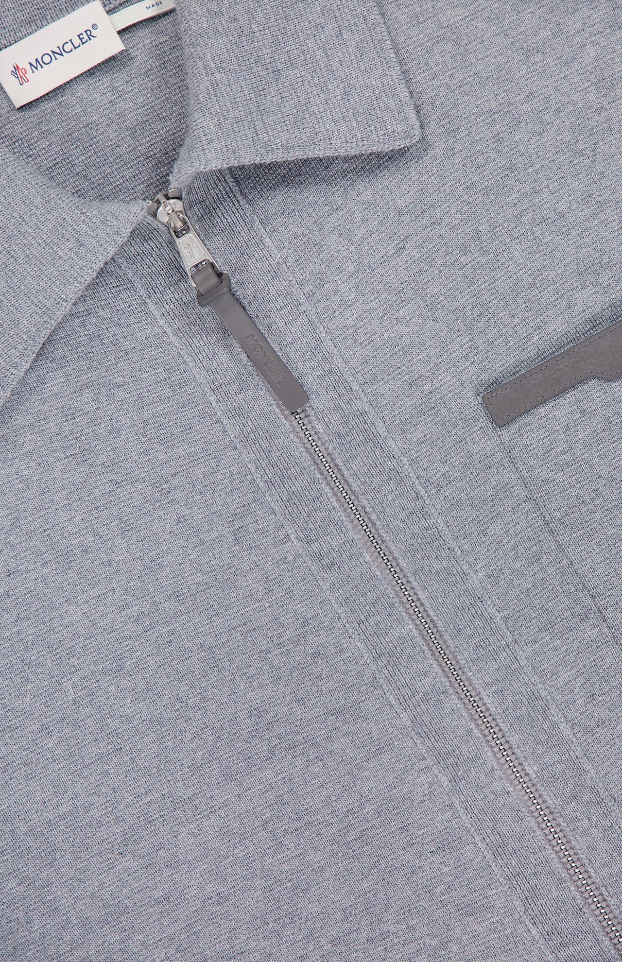 Close-up of the MONCLER Knit Zip Up Overshirt in light gray, featuring a silver zipper, textured fabric, partial chest pocket, and visible brand label inside the collar.