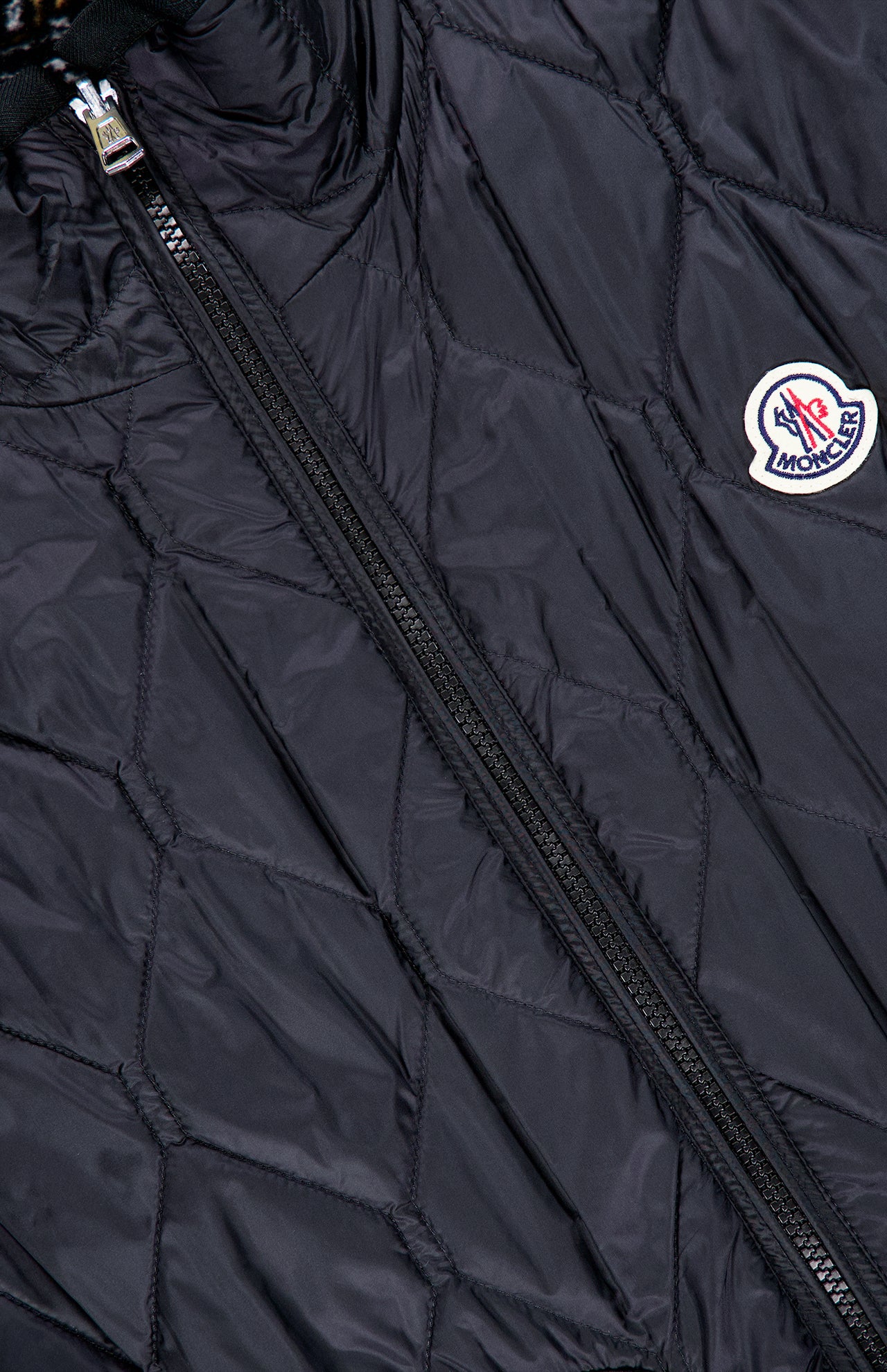 Close-up of a black MONCLER Reversible Paisley Fleece Vest featuring a visible zipper and a round Moncler logo patch on the right side. The fabric has a slight sheen with diamond-patterned stitching, accentuating the signature craftsmanship of this reversible vest.