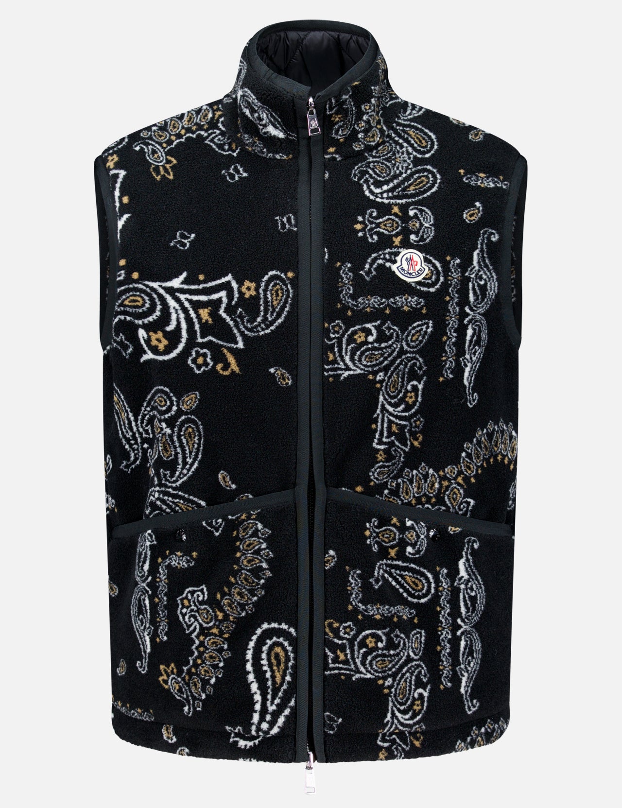 The MONCLER Reversible Paisley Fleece Vest features a black, white, and tan paisley pattern in a sleeveless teddy fleece design. It includes a front zipper closure, high collar, two large front pockets, and is finished with the Moncler logo patch on the left chest. Offering both style and versatility, this standout vest can be worn on either side.