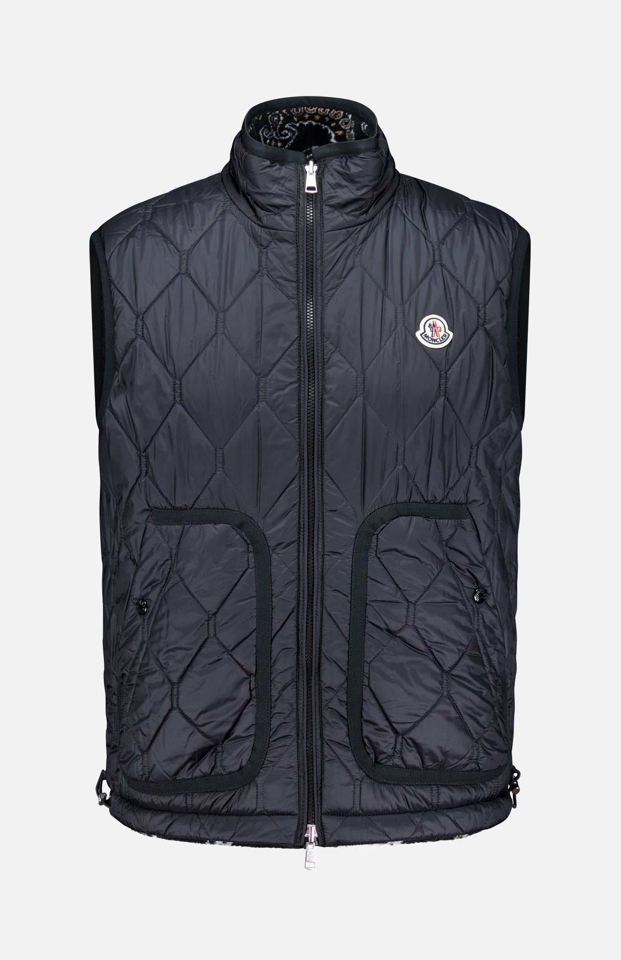 Introducing the MONCLER Reversible Paisley Fleece Vest: a black quilted sleeveless vest featuring a stylish front zipper, two spacious front pockets, and a small circular logo on the left chest. Designed with a high collar and an adjustable drawstring at the hem, this versatile piece draws inspiration from the iconic Moncler padded vest while showcasing reversible paisley fleece for modern flair.