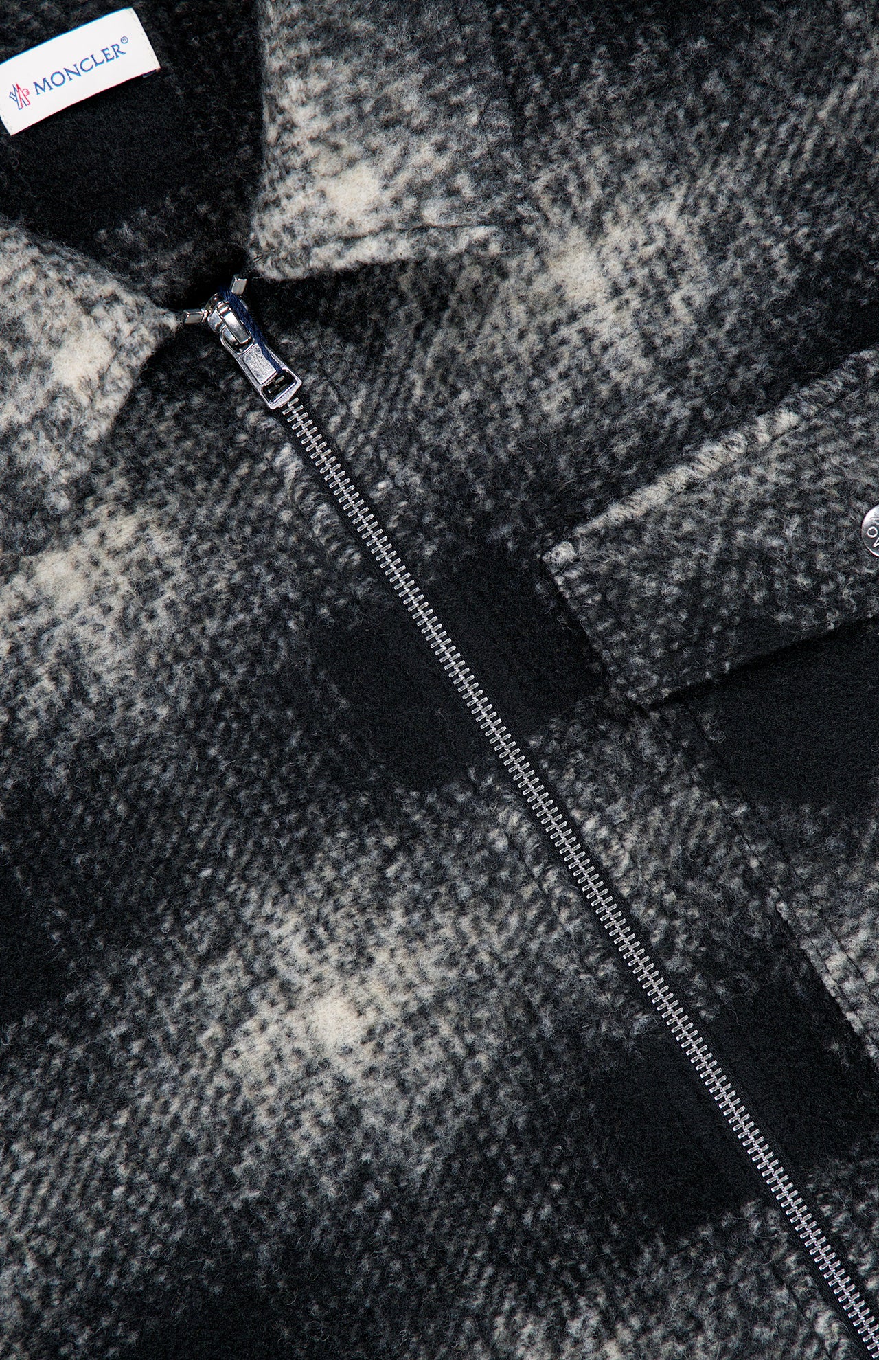 Close-up of the MONCLER Plaid Two-way Zip Overshirt, featuring a black and white plaid pattern, visible zipper, buttoned chest pocket, and the MONCLER label near the collar. The textured, slightly fuzzy fabric enhances this men’s casual outerwear piece with effortless style.
