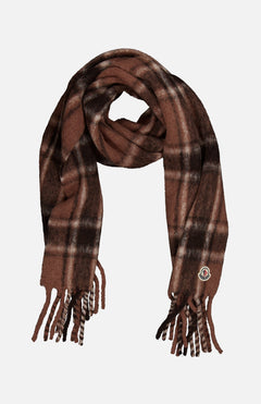 The MONCLER Plaid Fringed Scarf features a brown plaid pattern, fringed ends, and a small circular logo patch on one side. Crafted from an ultra-soft alpaca blend for extra warmth and style, it is displayed against a plain white background.