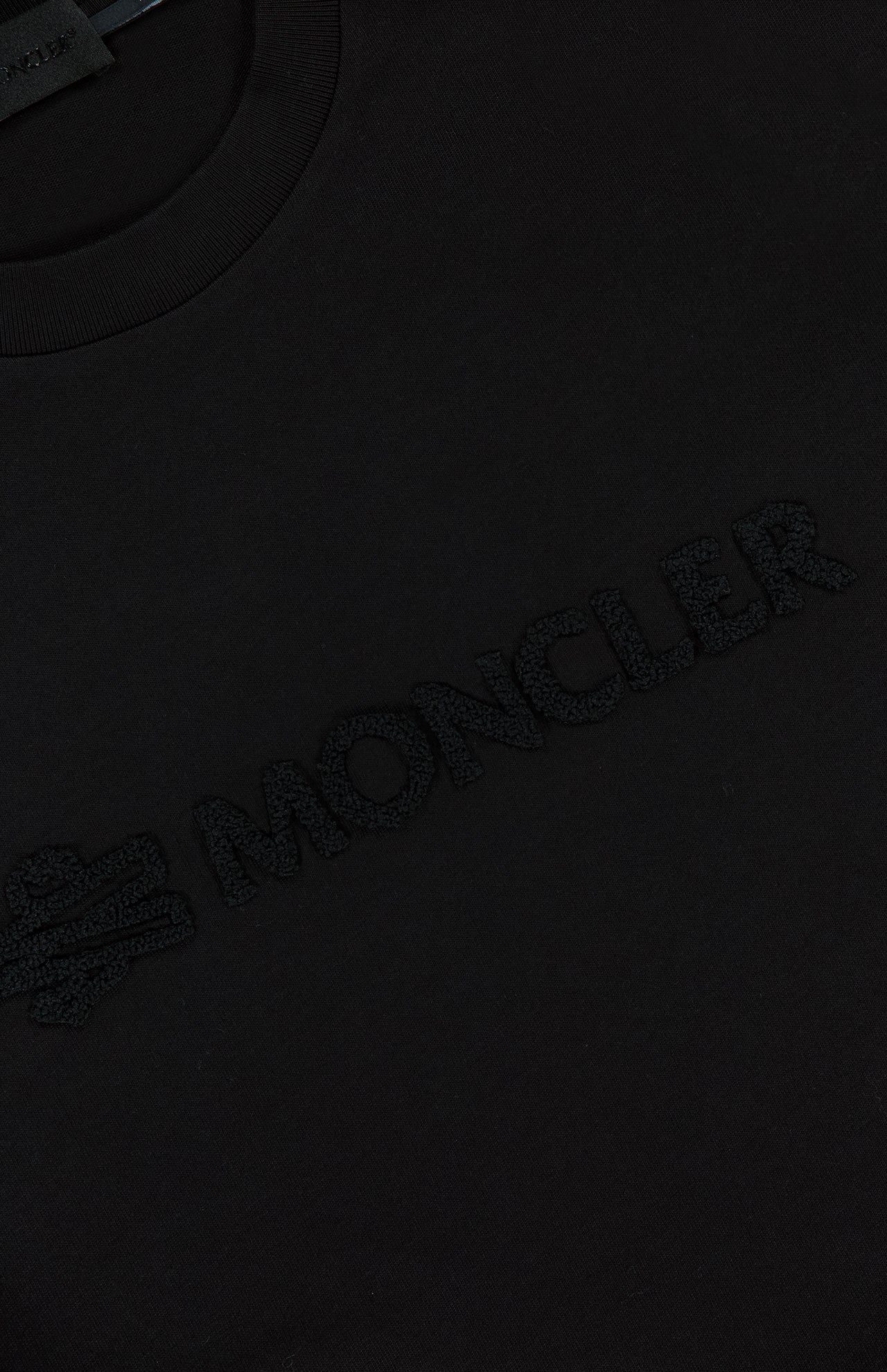 Close-up of the MONCLER Short Sleeve Logo T-Shirt in black, showcasing a subtle 3D embroidered logo and text on the chest for a textured look.