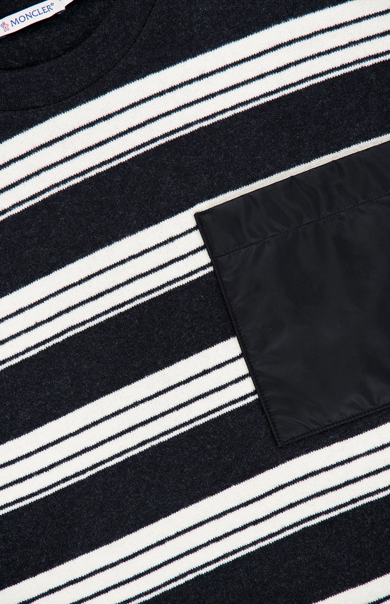 Close-up of the MONCLER Striped Long Sleeve T-Shirt, featuring black, white, and gray horizontal stripes and a solid black rectangular pocket on the right side, exemplifying designer outerwear style.