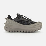 A side view of the MONCLER Trailgrip GTX Low Top Sneakers in gray and black, featuring a chunky Vibram tread sole for grip, a lace-up design, and the Moncler logo on the front side.