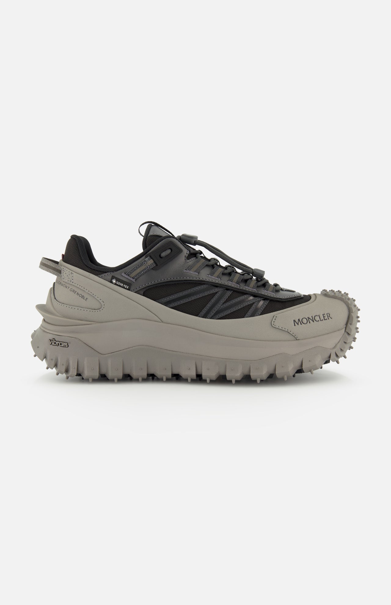 A side view of the MONCLER Trailgrip GTX Low Top Sneakers in gray and black, featuring a chunky Vibram tread sole for grip, a lace-up design, and the Moncler logo on the front side.
