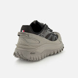 A close-up rear view of the MONCLER Trailgrip GTX Low Top Sneakers in gray and black, featuring a lugged Vibram sole, nylon upper, and a small French flag on the heel, set against a plain white background.