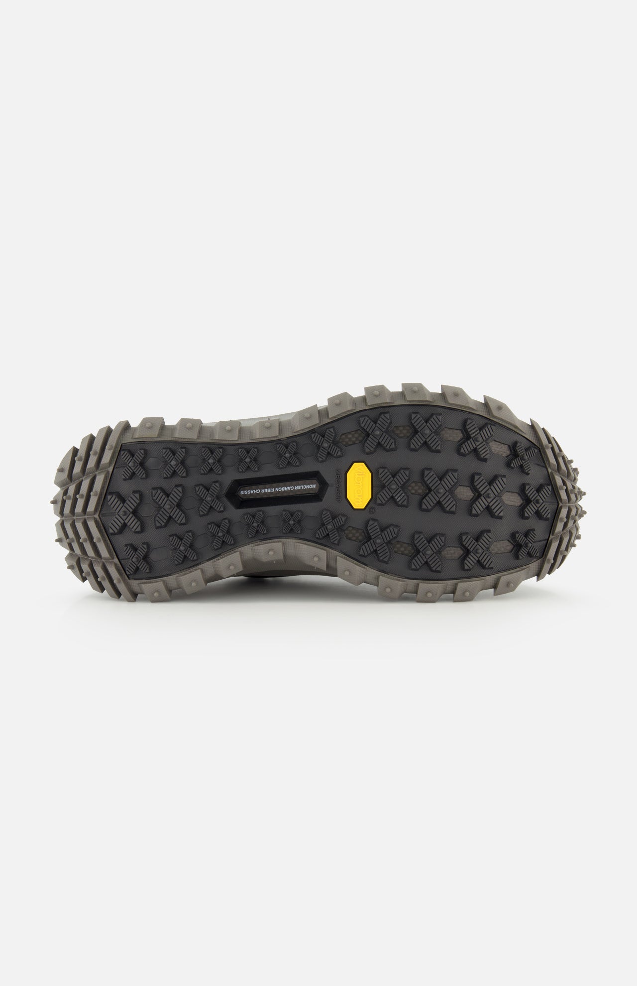 The image shows the bottom view of MONCLER Trailgrip GTX Low Top Sneakers with a rugged black Vibram sole, deep patterned treads for traction, and a yellow logo near the center.