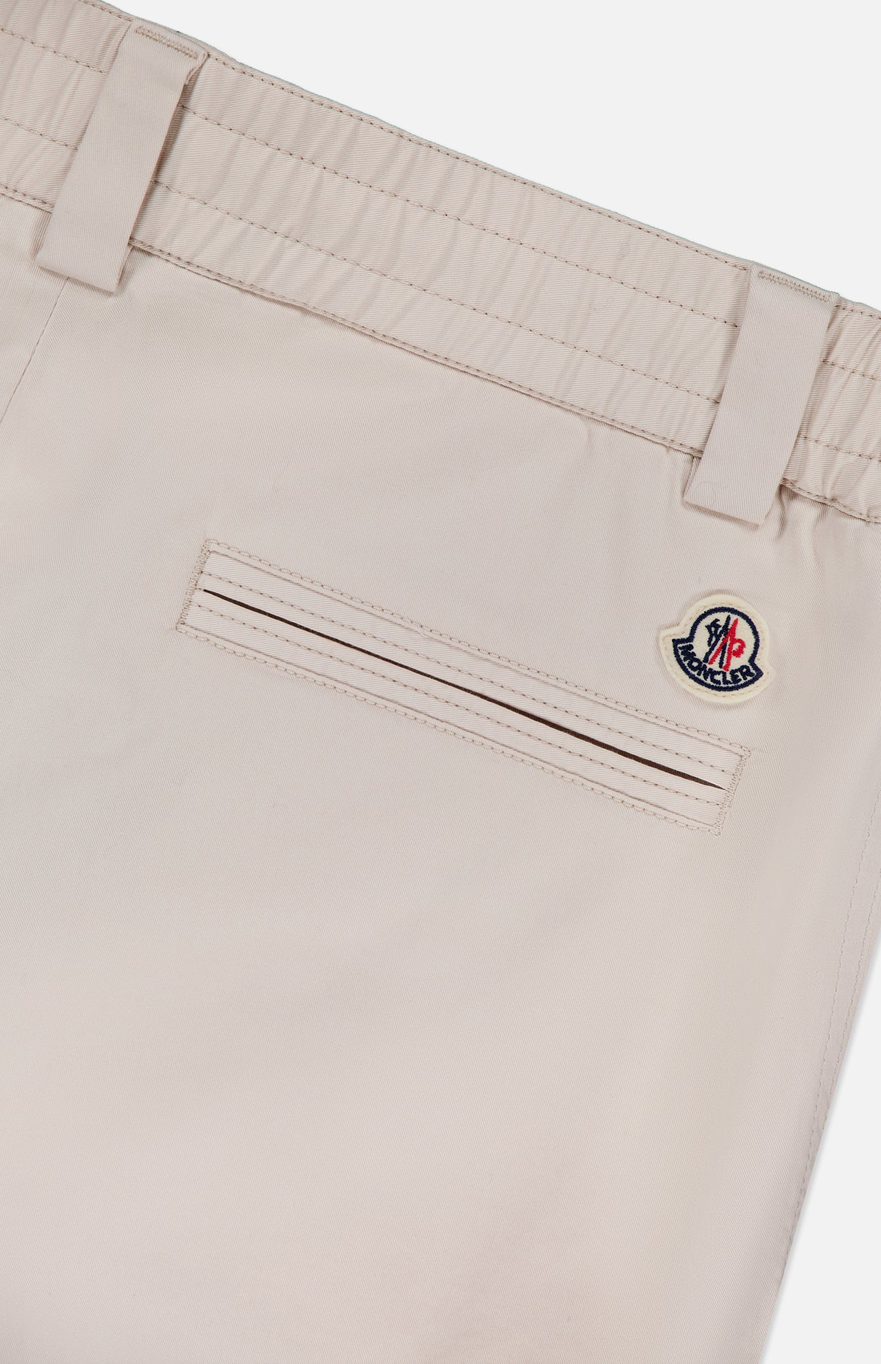 Close-up of MONCLER Drawstring Stretch Cotton Trousers highlights a horizontal back pocket, belt loops, elastic waistband with drawstring, and a small circular Moncler logo patch above the pocket.