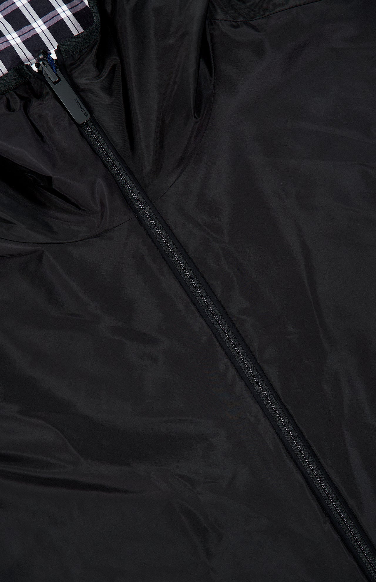 Close-up of the MONCLER Vandelli Reversible Plaid Jacket in black, featuring a lightweight design with a central zipper. The top inner lining displays a black, white, and purple plaid pattern.