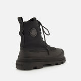 The MONCLER Vera Sheal Ankle Boots feature a black lace-up design with a thick, rugged sole, textured laces, and a circular logo patch on the side. Perfect for city living, these ankle boots are photographed angled to showcase their side and back against a white background.