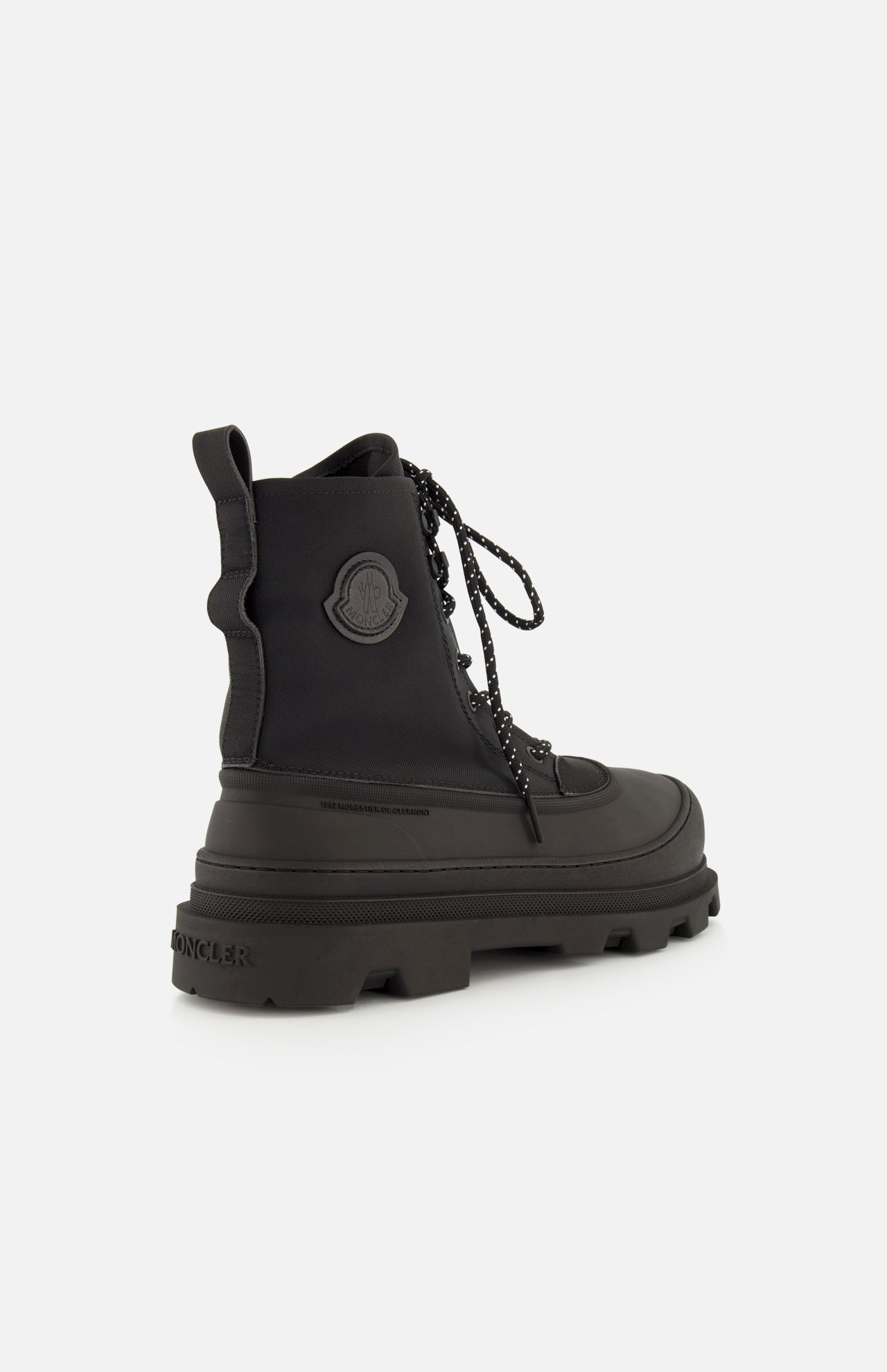 The MONCLER Vera Sheal Ankle Boots feature a black lace-up design with a thick, rugged sole, textured laces, and a circular logo patch on the side. Perfect for city living, these ankle boots are photographed angled to showcase their side and back against a white background.