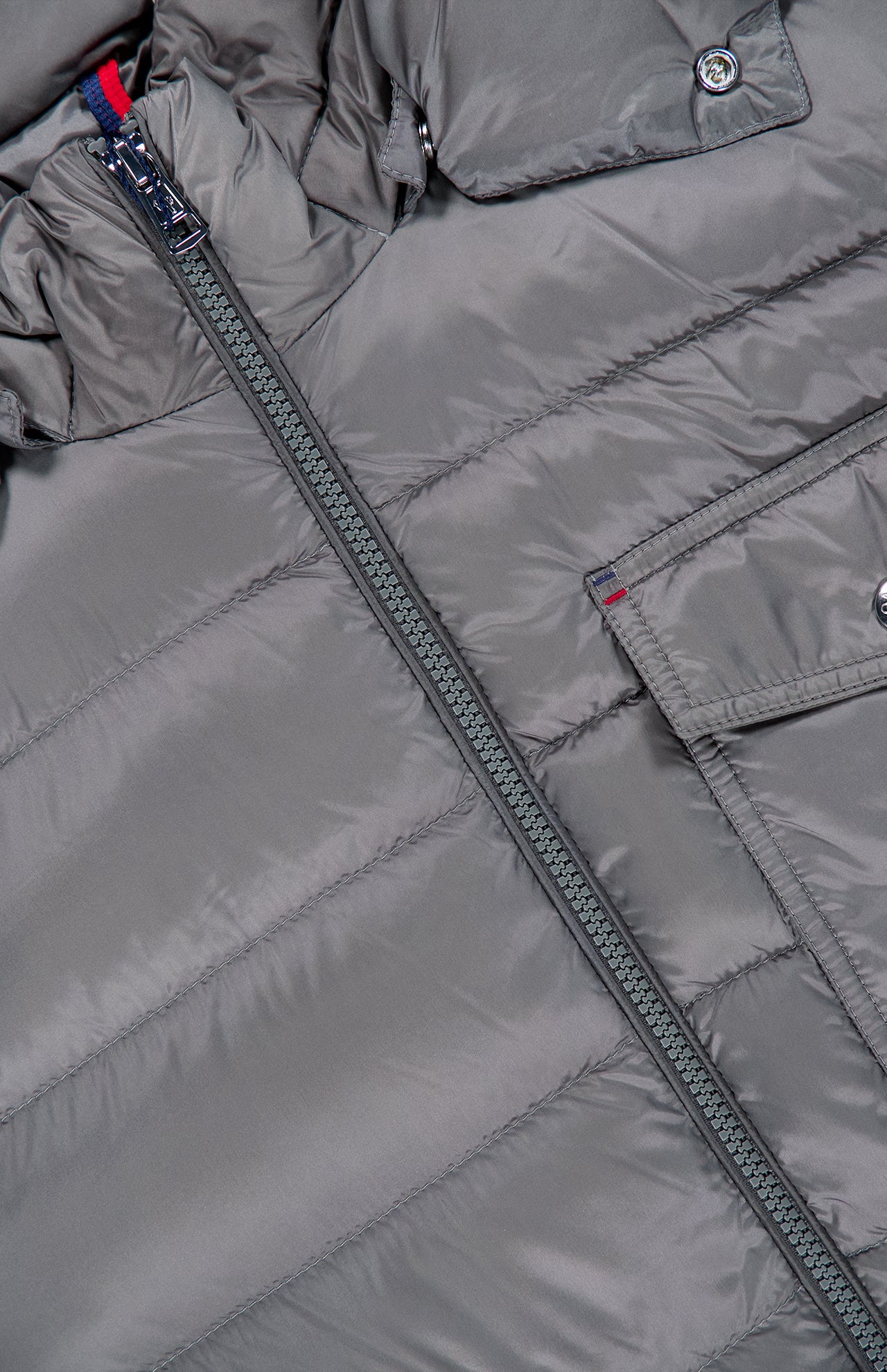 Close-up of the Verith Puffer Jacket by MONCLER in gray, highlighting its diagonal zipper, horizontal stitching, and a flap pocket with a metal snap button—evoking the signature style of Moncler’s iconic puffer jackets.