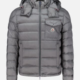 A gray MONCLER Verith Puffer Jacket with a front zipper, hood, chest pocket featuring a logo patch, and elastic cuffs is displayed on a plain white background. This lightweight down jacket offers added versatility and comfort with its removable hood.