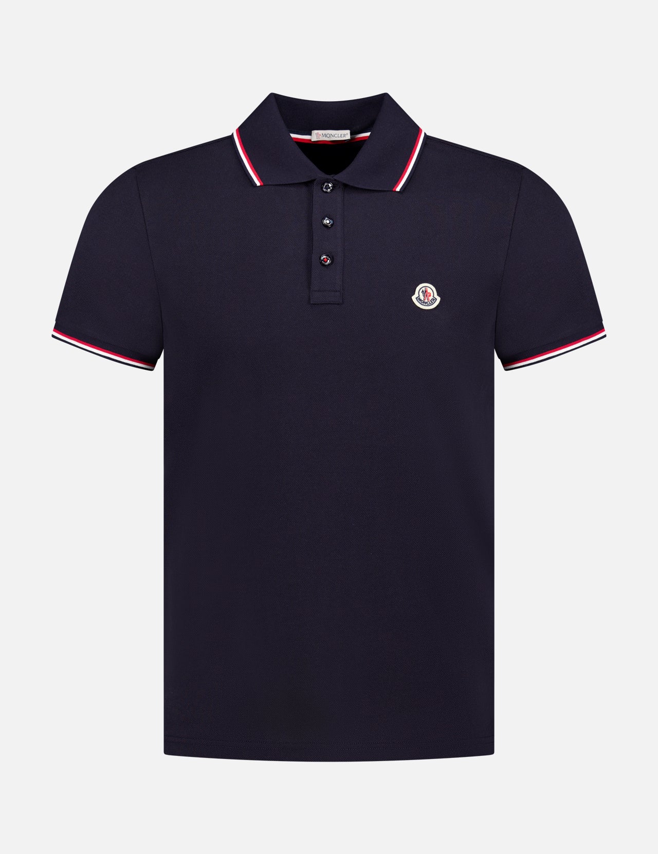 The MONCLER Piquet Short Sleeve Polo Shirt is a navy cotton men's polo with a collar, three buttons, white and red trim, and a small embroidered circular logo patch on the chest—signature to Moncler’s classic style.