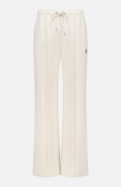 The MONCLER Drawstring Sweat Bottoms feature a cream color, wide-leg fit, elastic drawstring waistband, side seams, front vertical stitching, and a small logo patch on the upper left thigh—ideal for luxe après-ski or casual wear.