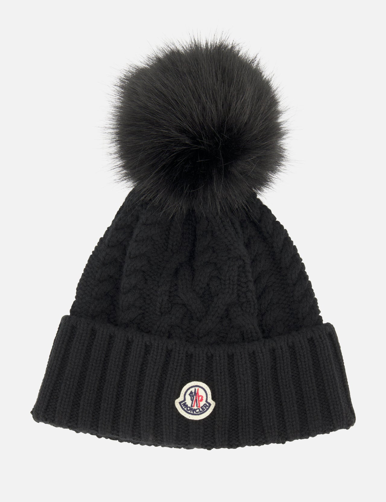 A black MONCLER Cableknit Pom Beanie featuring a large faux fur pom pom on top, a ribbed folded brim, and a round Moncler logo patch.