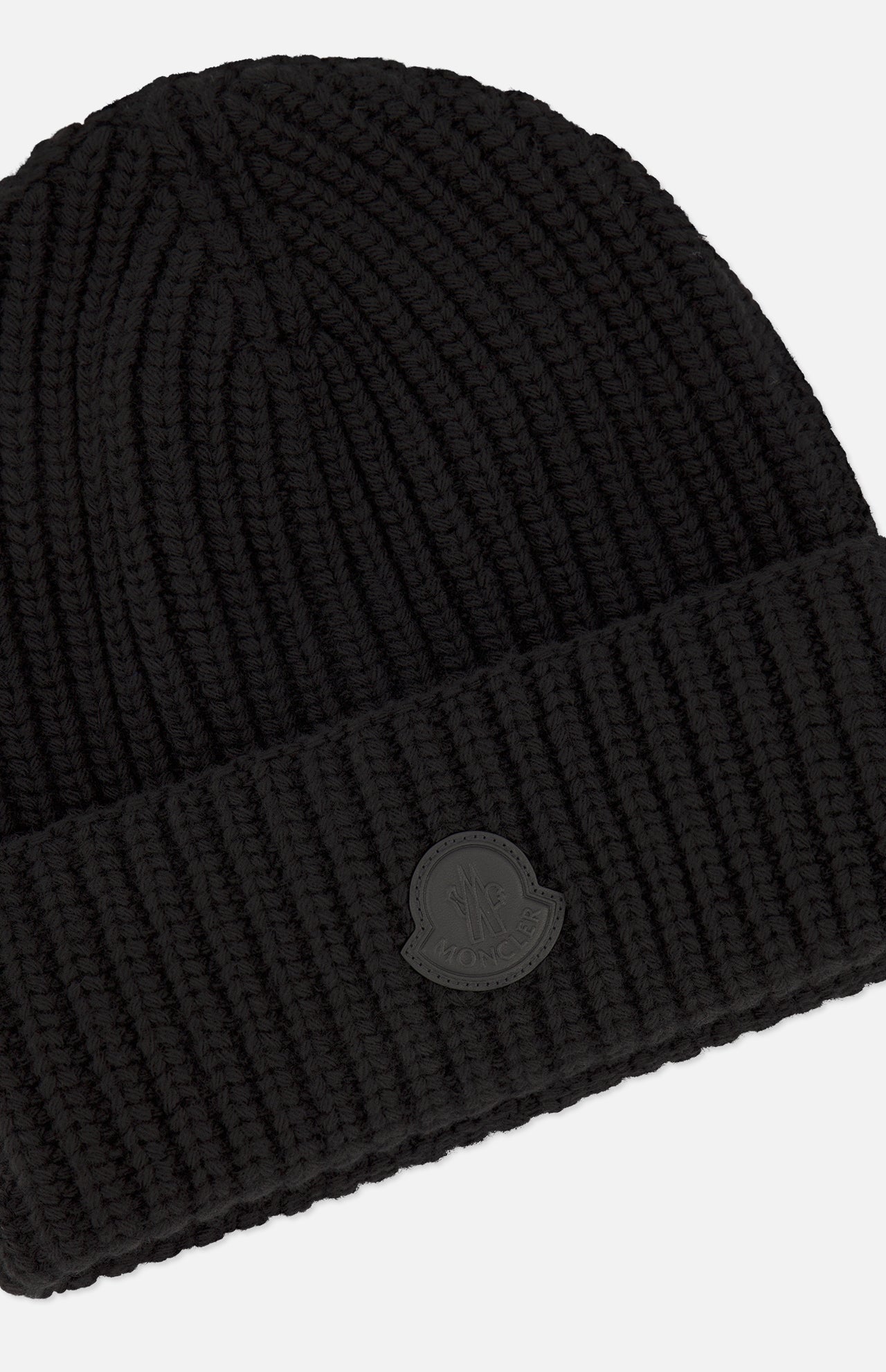The MONCLER Tonal Logo Beanie is crafted from premium virgin wool cashmere in black, featuring a ribbed knit design with a folded cuff and a subtle round logo patch on the front. Showcasing a chunky texture, this beanie offers a simple and classic aesthetic.