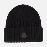 A black Tonal Logo Beanie by MONCLER, crafted from luxurious virgin wool cashmere with a wide folded cuff and a round tonal embossed logo patch on the front, photographed against a plain white background.