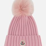 Introducing the MONCLER Ribbed Pom Beanie—crafted in pink ribbed knit with a large, fluffy faux fur pom pom on top and a folded brim accented by a small embroidered logo patch at the front.