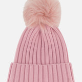 The MONCLER Ribbed Pom Beanie features a pink ribbed knit design with a folded brim and is topped with a large, fluffy faux fur pom pom. Photographed against a plain white background, this beanie combines cozy warmth and playful style for your winter wardrobe.