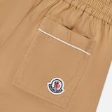 Close-up of MONCLER Brushed Techno Cotton Shorts in beige, featuring an elastic waistband, a large back pocket with white trim, and a Moncler logo patch on the pocket.