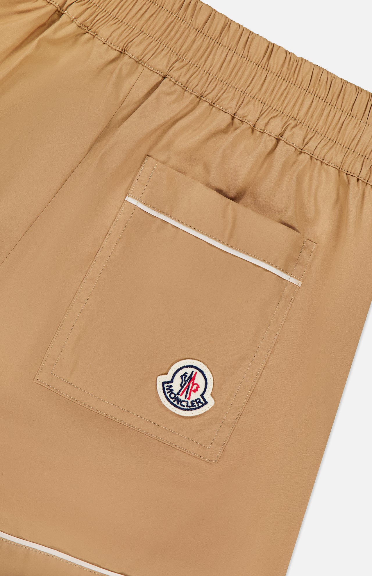 Close-up of MONCLER Brushed Techno Cotton Shorts in beige, featuring an elastic waistband, a large back pocket with white trim, and a Moncler logo patch on the pocket.