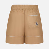 MONCLER Brushed Techno Cotton Shorts in beige feature an elastic waistband, a single back pocket with a logo patch, and white trim on the pocket and hems. Tailored design inspired by Moncler’s high-performance outerwear, shown on a white background.