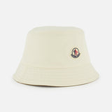 The MONCLER Reversible Bucket Hat in cream features subtle stitching and a small front logo patch, showcased on a plain white background—a stylish piece that echoes the brand’s outerwear heritage.