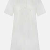The MONCLER Embroidered Mini Dress is a short-sleeved, knee-length white shirtdress with front buttons, pointed collar, subtle chest floral embroidery, and an elegant A-line silhouette for timeless appeal.