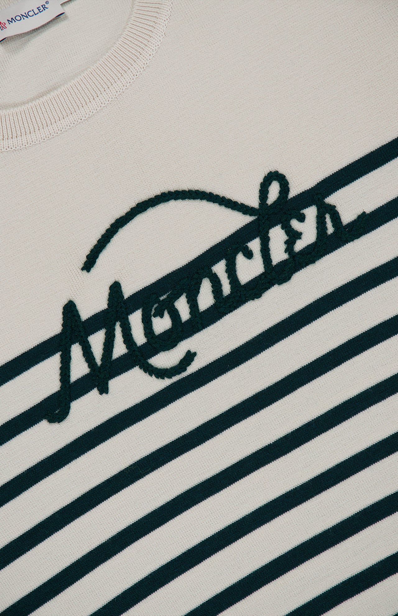 Close-up of the MONCLER Extrafine Wool Crewneck Sweater, crafted from extra-fine cream-colored wool and accented with dark green nautical stripes and large Moncler embroidery across the chest.