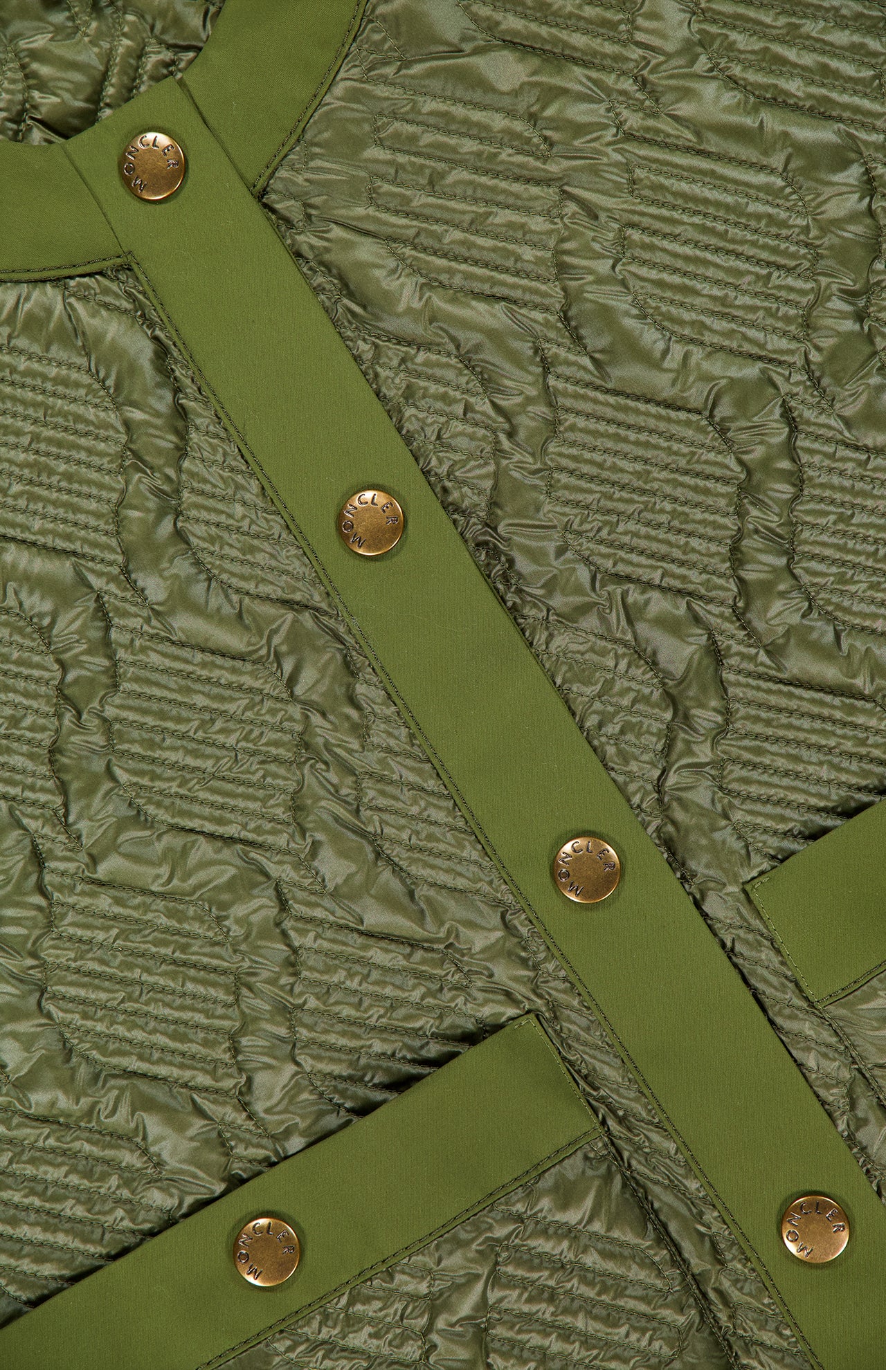Close-up of quilted olive green fabric from the MONCLER Libellule Water Repellent Quilted Jacket, featuring textured stitching, gold snap buttons, and smooth trim that highlight this feminine puffer down jacket’s luxurious details.