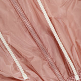Close-up of the MONCLER Liriope Hooded Rain Jacket in pink, featuring a textured waistband, central zipper, and two white drawstrings with plastic tips. The shiny, slightly wrinkled fabric emphasizes its stylish, high-performance design.