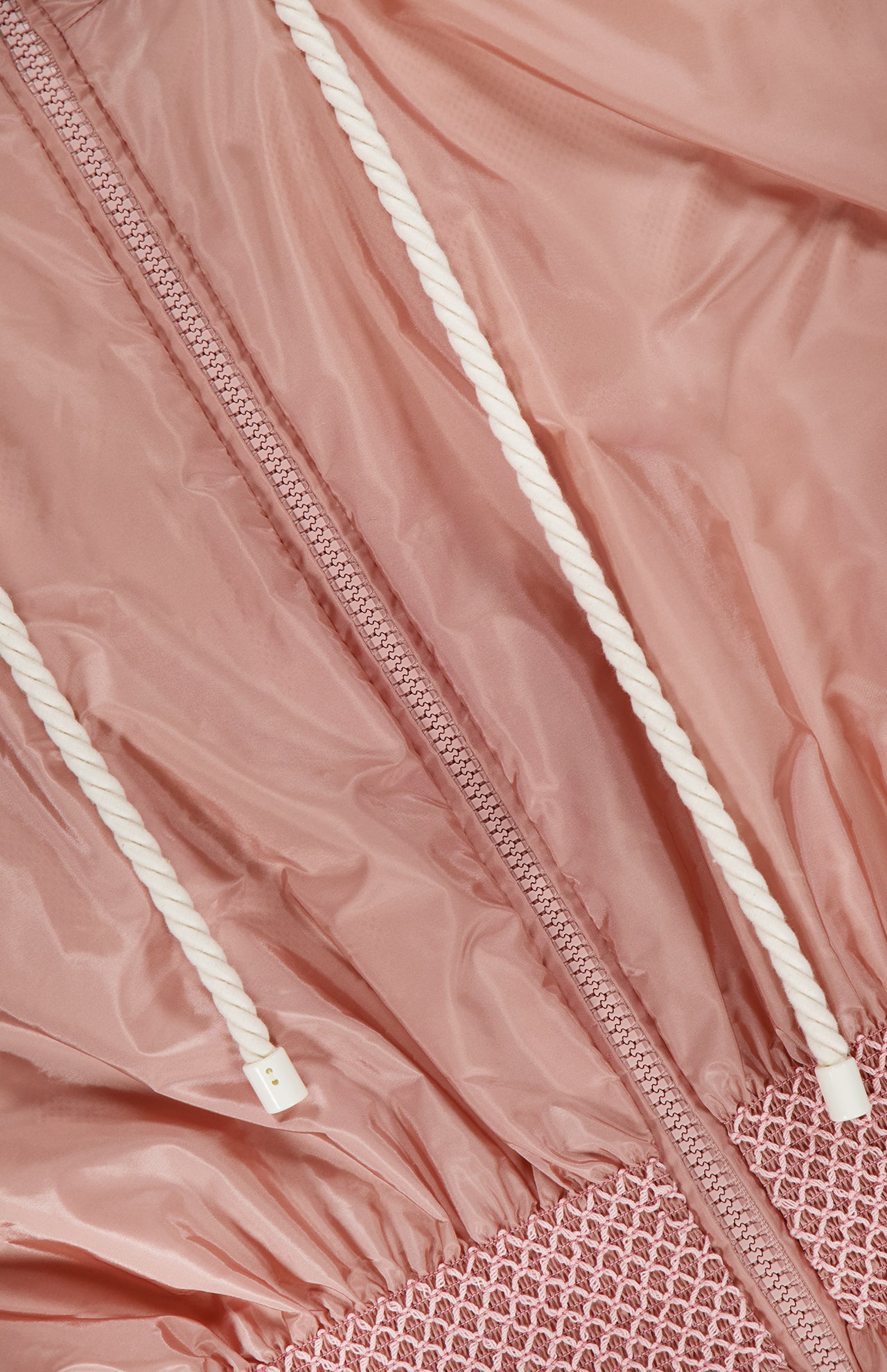 Close-up of the MONCLER Liriope Hooded Rain Jacket in pink, featuring a textured waistband, central zipper, and two white drawstrings with plastic tips. The shiny, slightly wrinkled fabric emphasizes its stylish, high-performance design.