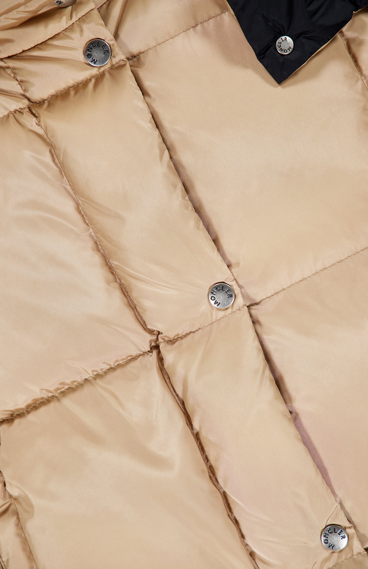 Close-up of the Macareux Down Puffer Vest by MONCLER in beige, featuring a shiny, padded finish with visible stitching outlining its square quilted pattern. The design showcases metallic snap buttons, some engraved, and combines lightweight warmth with a practical water-repellent finish for stylish versatility.