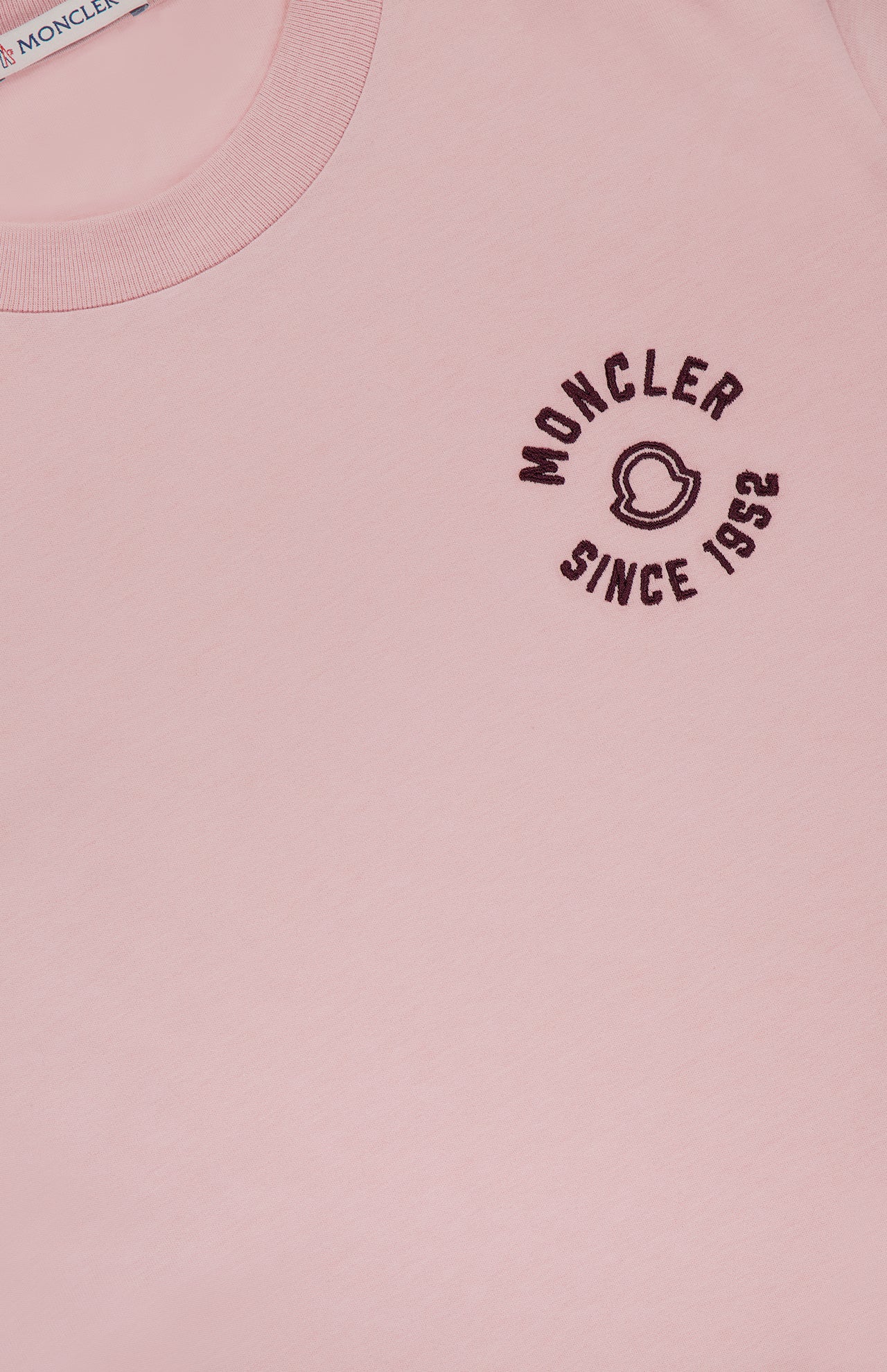 Close-up of a light pink MONCLER Short Sleeve T-Shirt, showcasing logo details and "MONCLER SINCE 1952" embroidered in black on the left chest, with a partial view of the inner collar label.
