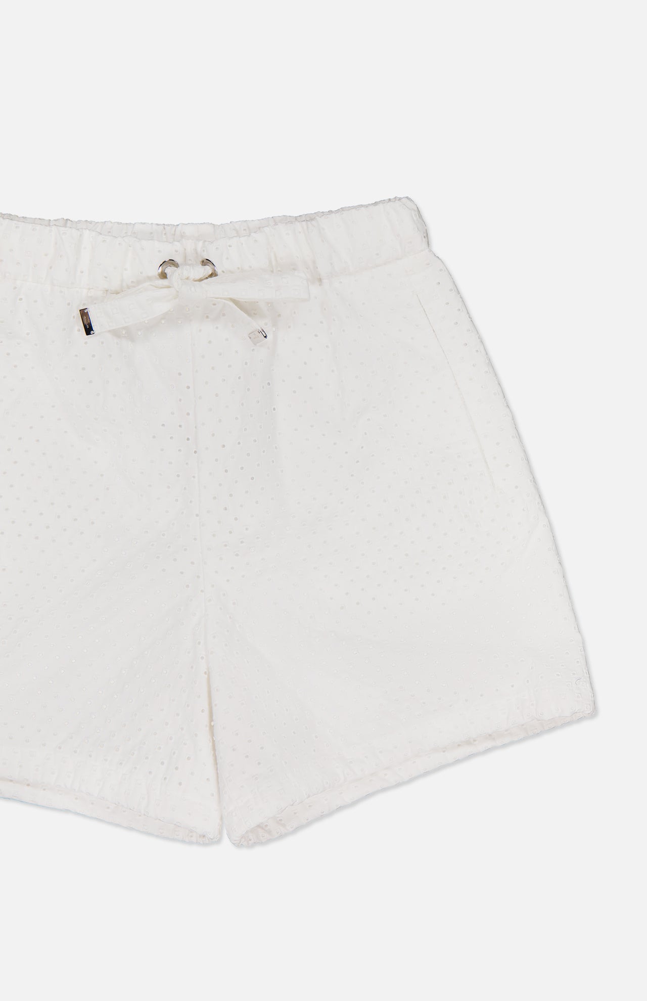 MONCLER Drawstring Eyelet Shorts in white feature an elastic waistband, drawstring tie, side pockets, and a delicate eyelet texture, showcased against a plain white background.