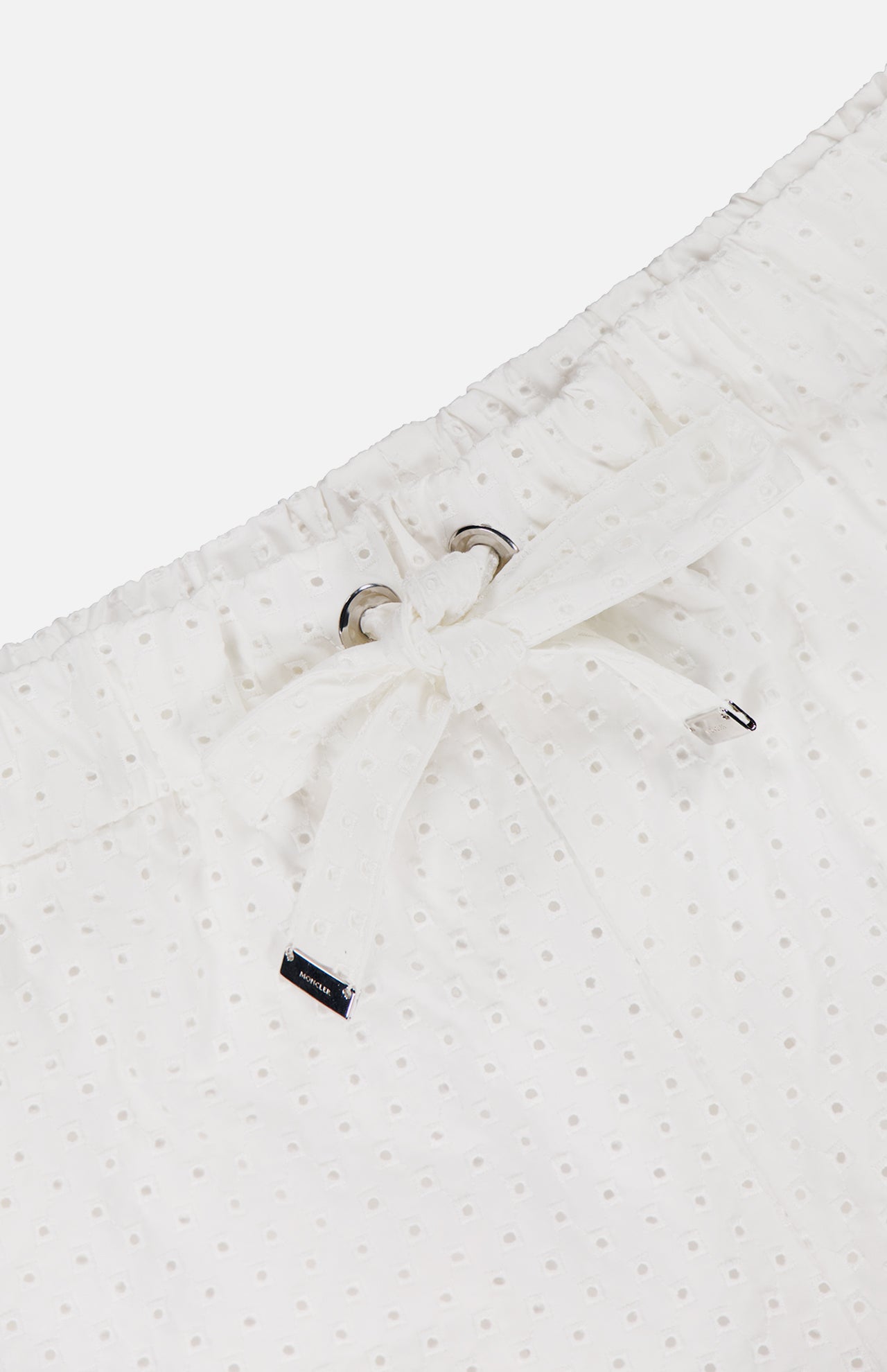 Close-up of the MONCLER Drawstring Eyelet Shorts’ white waistband with adjustable drawstring, silver grommets, and a branded metal tag detail at the end.