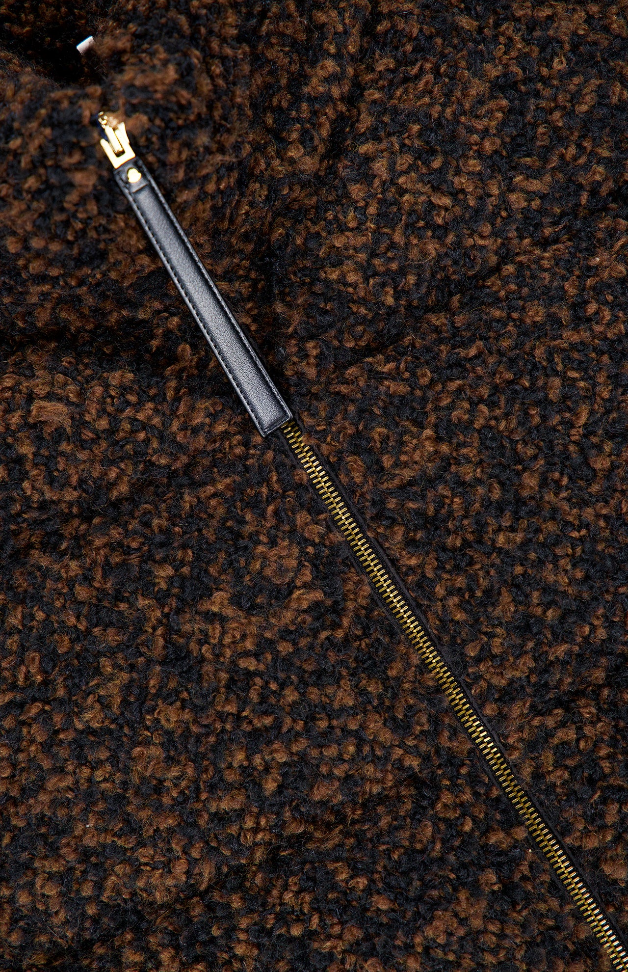A close-up of the brown and black textured wool fabric of the MONCLER Trascendance Tweed Jacket, showcasing a partially unzipped gold zipper with a black leather pull tab—an elegant detail characteristic of this sophisticated piece.