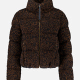 The MONCLER Trascendance Tweed Jacket is an elegant women’s outerwear piece, featuring a brown and black textured design with a high collar, front zipper, and long sleeves. Combining the warmth of a classic MONCLER down jacket with the sophisticated appeal of tweed, this jacket is displayed against a plain white background.