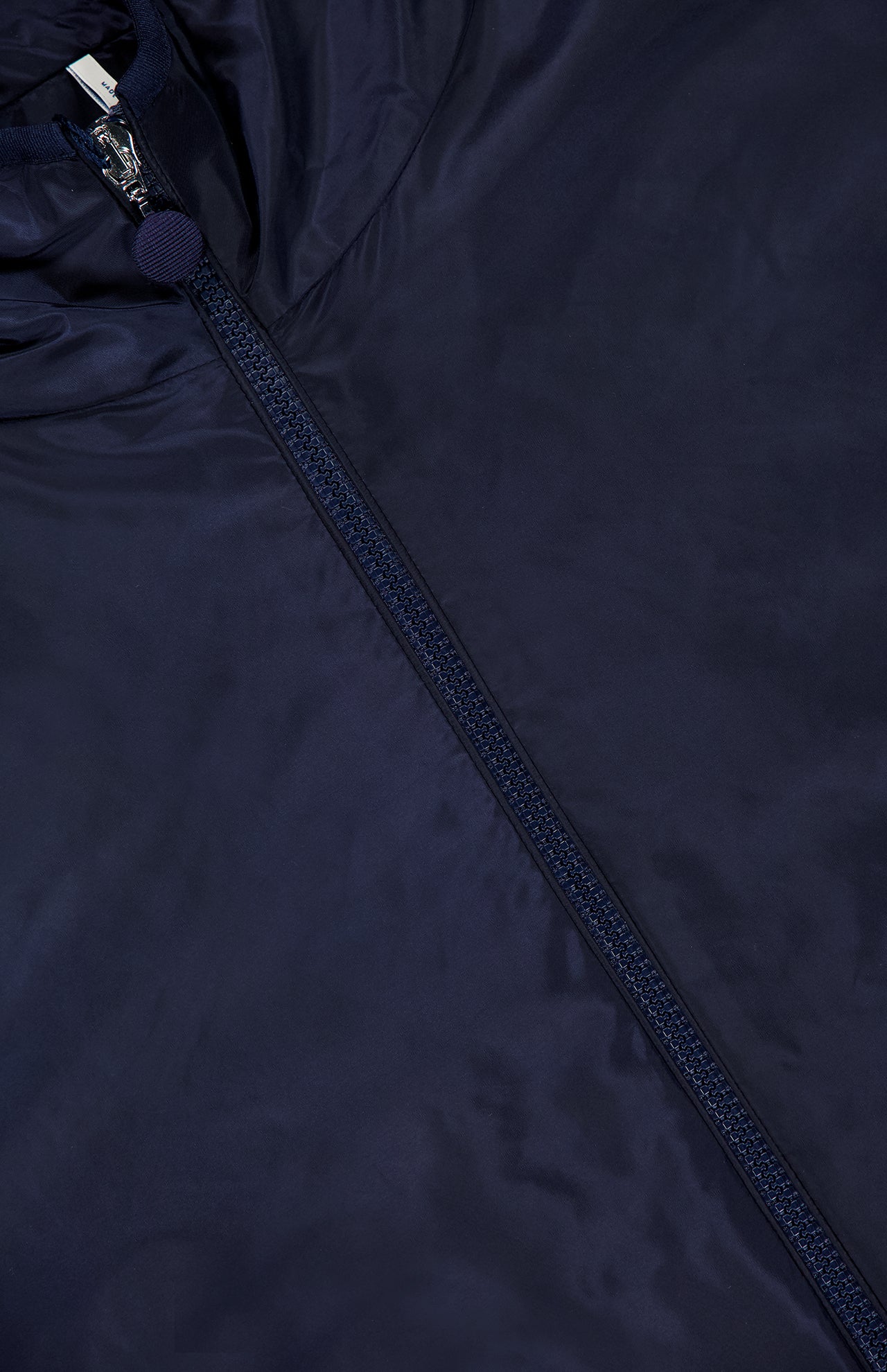 A close-up of the MONCLER Zelkova Embroidered Sleeves Jacket highlights its shiny navy fabric, distinctive zipper detail, and small round zipper pull near the top.