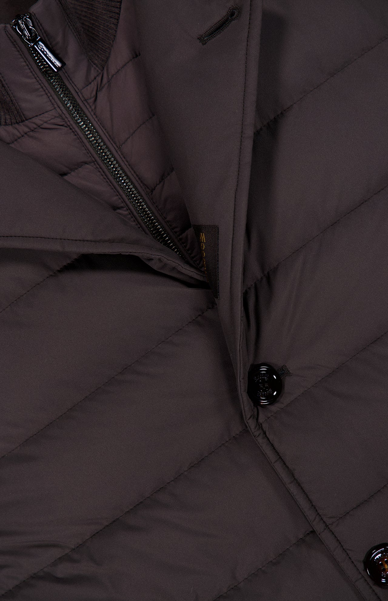 Close-up of the MOORER Sinardi Removable Bib Jacket, showing a black button, diagonal zipper, and detailed stitching on the dark brown fabric with a detachable puffer bib.