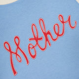 The Boxy Goodie Inset T-shirt by MOTHER is a light blue, 100% cotton shirt with cream trim and "Mother" stitched in bold red cursive across the front.