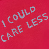 A close-up of The Sinful Slim T-shirt by MOTHER, a vintage-look red tee made from 100% cotton, featuring "I COULD CARE LESS" printed in bold light gray letters.