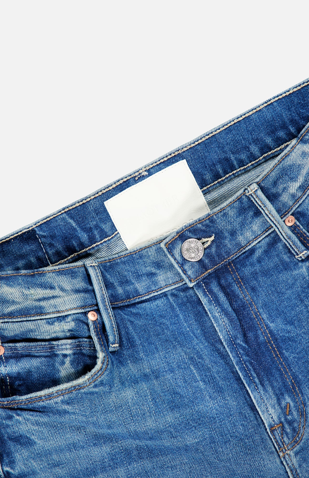 Close-up of the waistband and top section of MOTHER Lilrunaway Jeans in On A Roll, featuring a blank white label and visible button, shown against a light background.