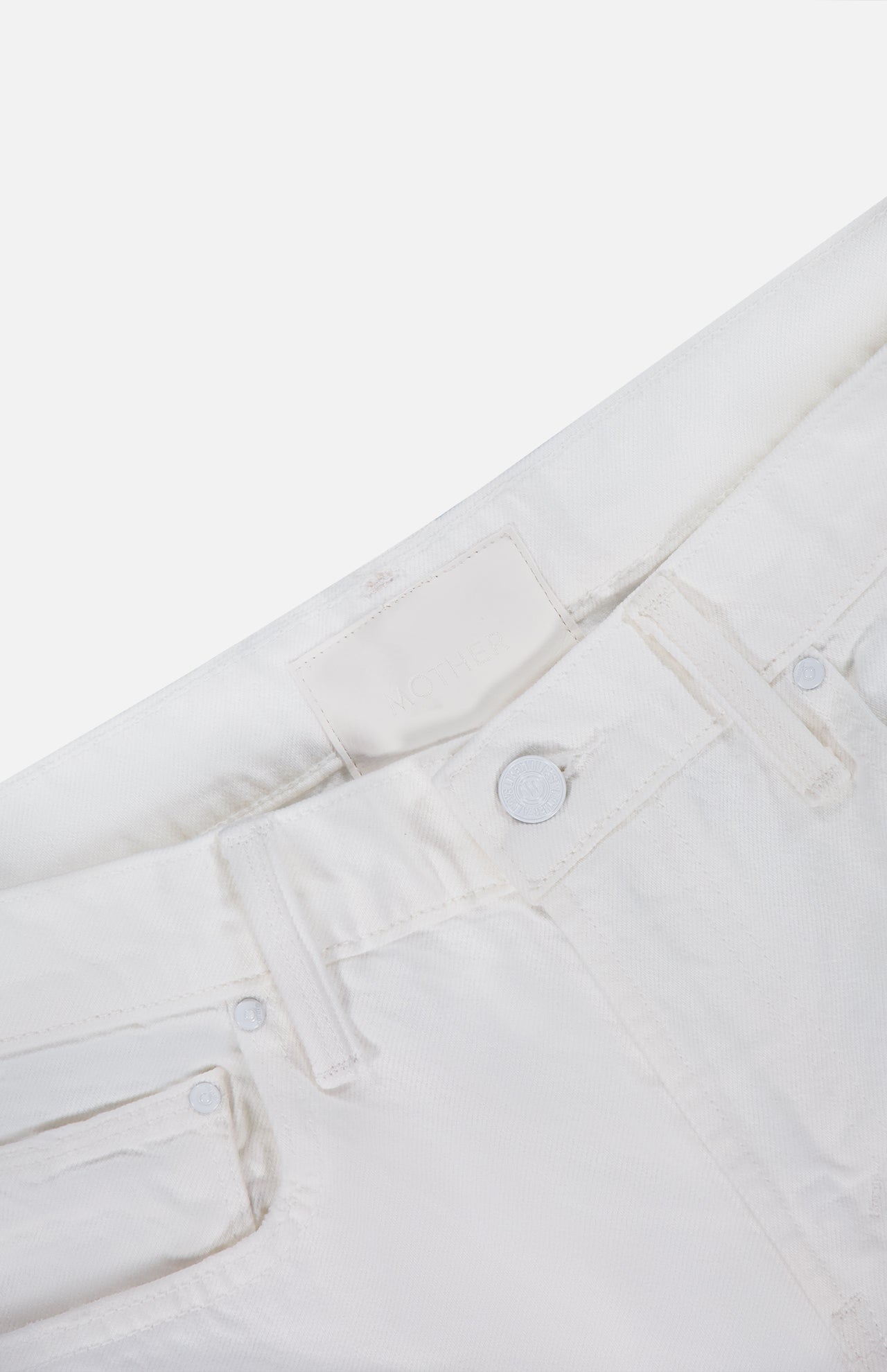 Close-up of the upper part of The Bookie Skimp Pant in Picket Fence by MOTHER, showing the waistband, belt loops, button, front pockets, and a blank white label on these classic mid-rise white denim jeans.
