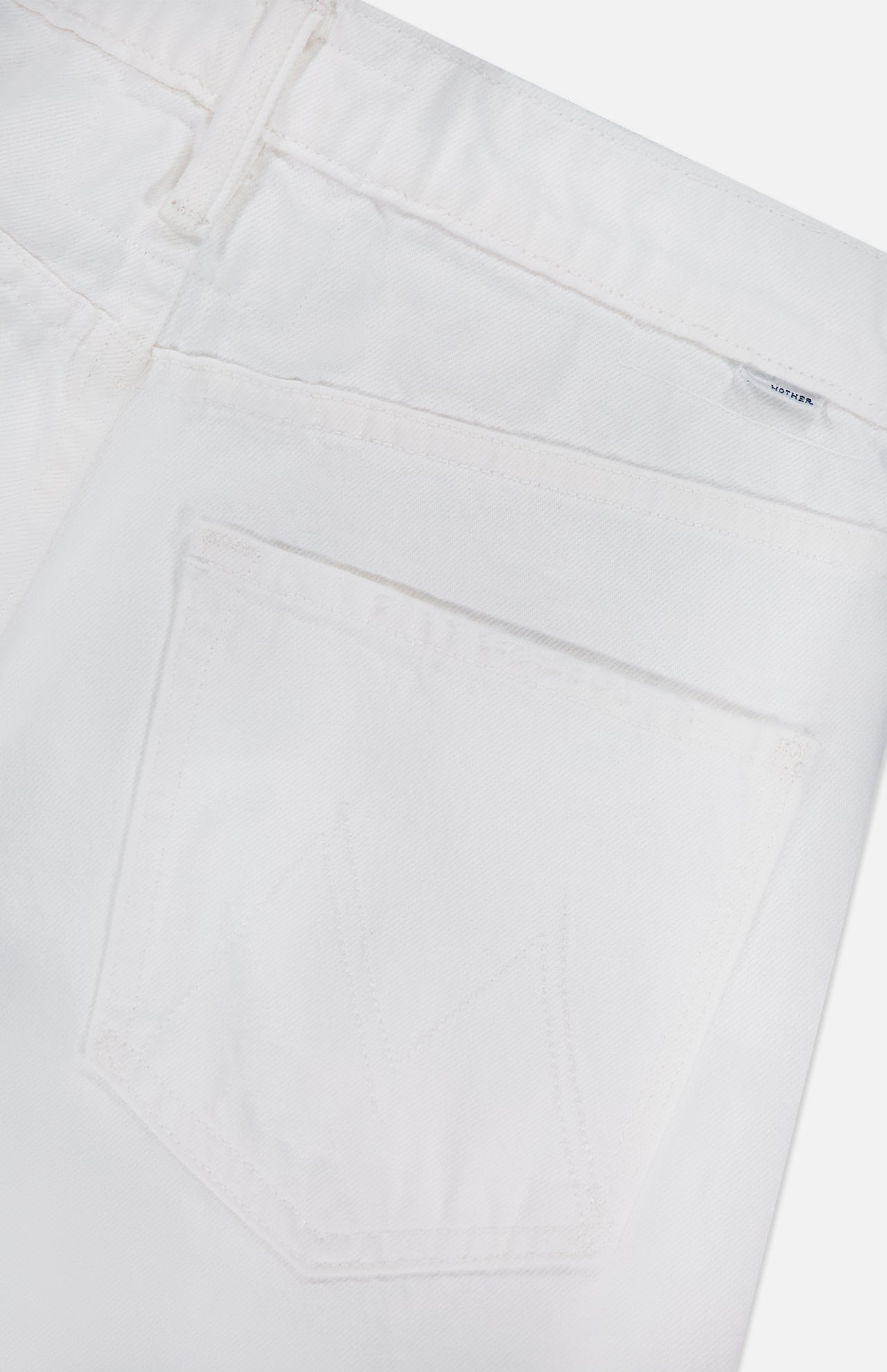 Close-up of the back pocket and waistband of MOTHER's The Bookie Skimp Pant in Picket Fence, featuring a small silver brand tag near the belt loop and subtle pocket stitching.