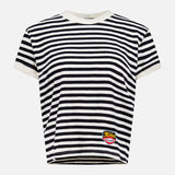 Introducing the Boxy Goodie Goodie T-shirt by MOTHER—a short-sleeved crew neck tee with bold black and white stripes, designed for a relaxed boxy fit. Crafted from 100% cotton, it features a crisp white collar and sleeve trim along with a small, colorful patch sewn near the bottom left hem.