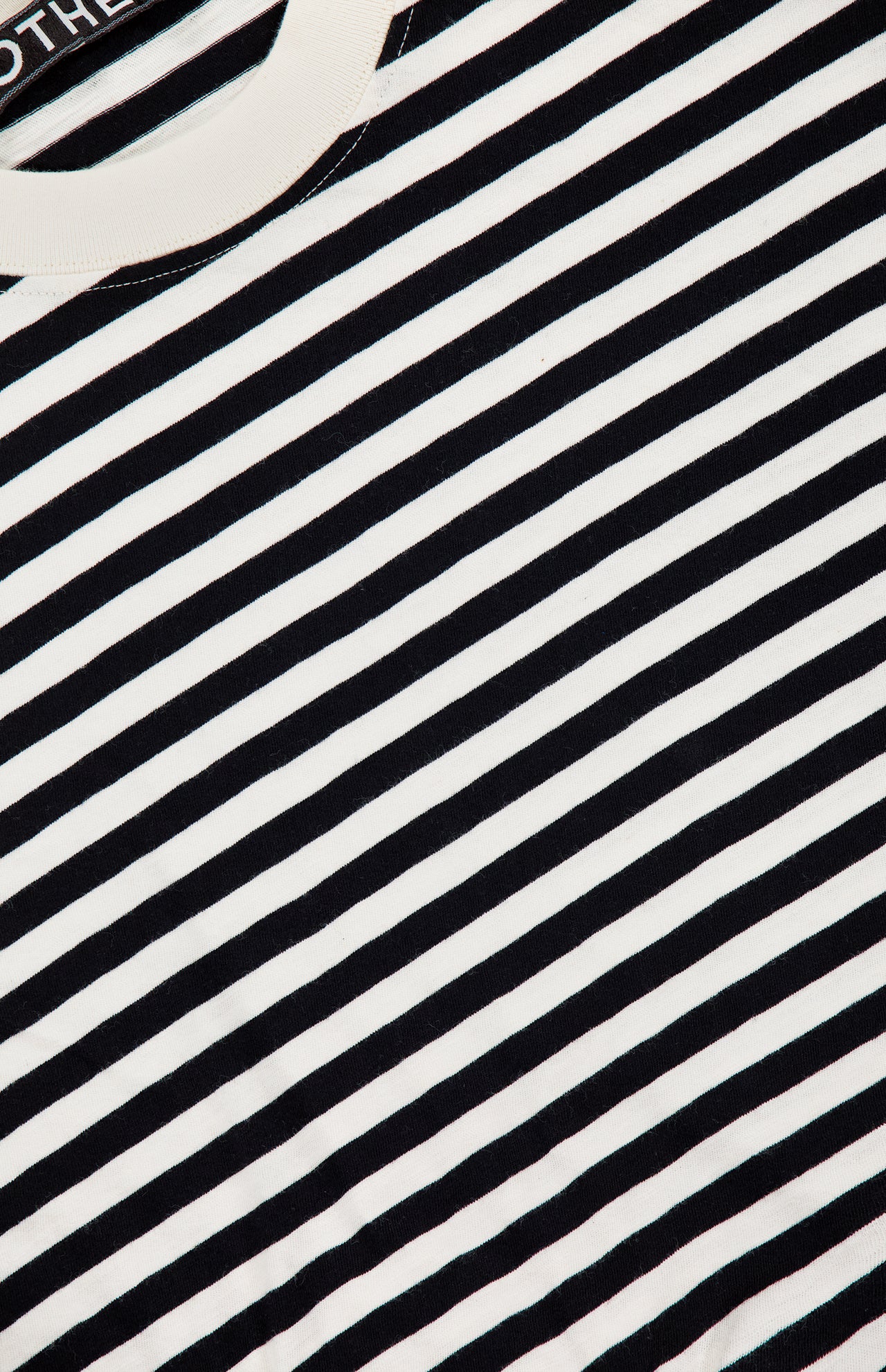 A close-up view of The Boxy Goodie Goodie T-shirt by MOTHER, featuring black and white horizontal stripes, with the crew neck collar and part of the neck label visible at the top left corner.