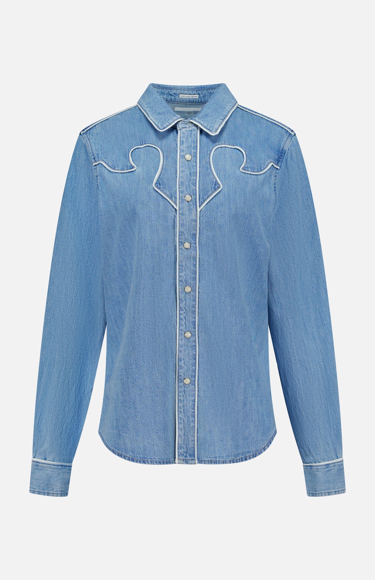 The Country Exe’s Shirt by MOTHER is an oversized, light blue denim shirt featuring long sleeves, a pointed collar, snap button closure, and white stitched decorative details along the chest and seams. Displayed on a plain white background, this classic western button-up brings timeless charm to any wardrobe.